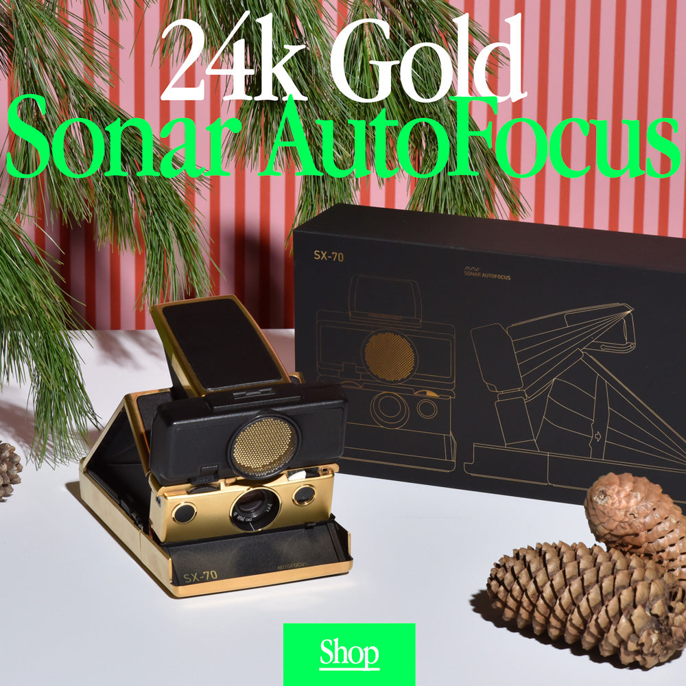 24k gold sonar autofocus polaroid folding camera with its box under pine tree 